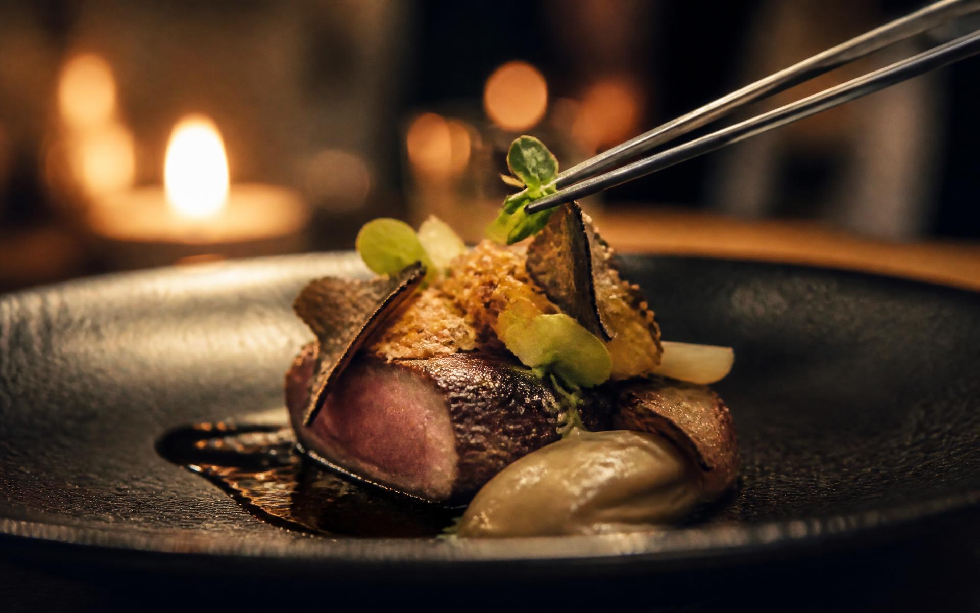 Close macro of a fine-dining plated course being finished with tweezers by candlelight