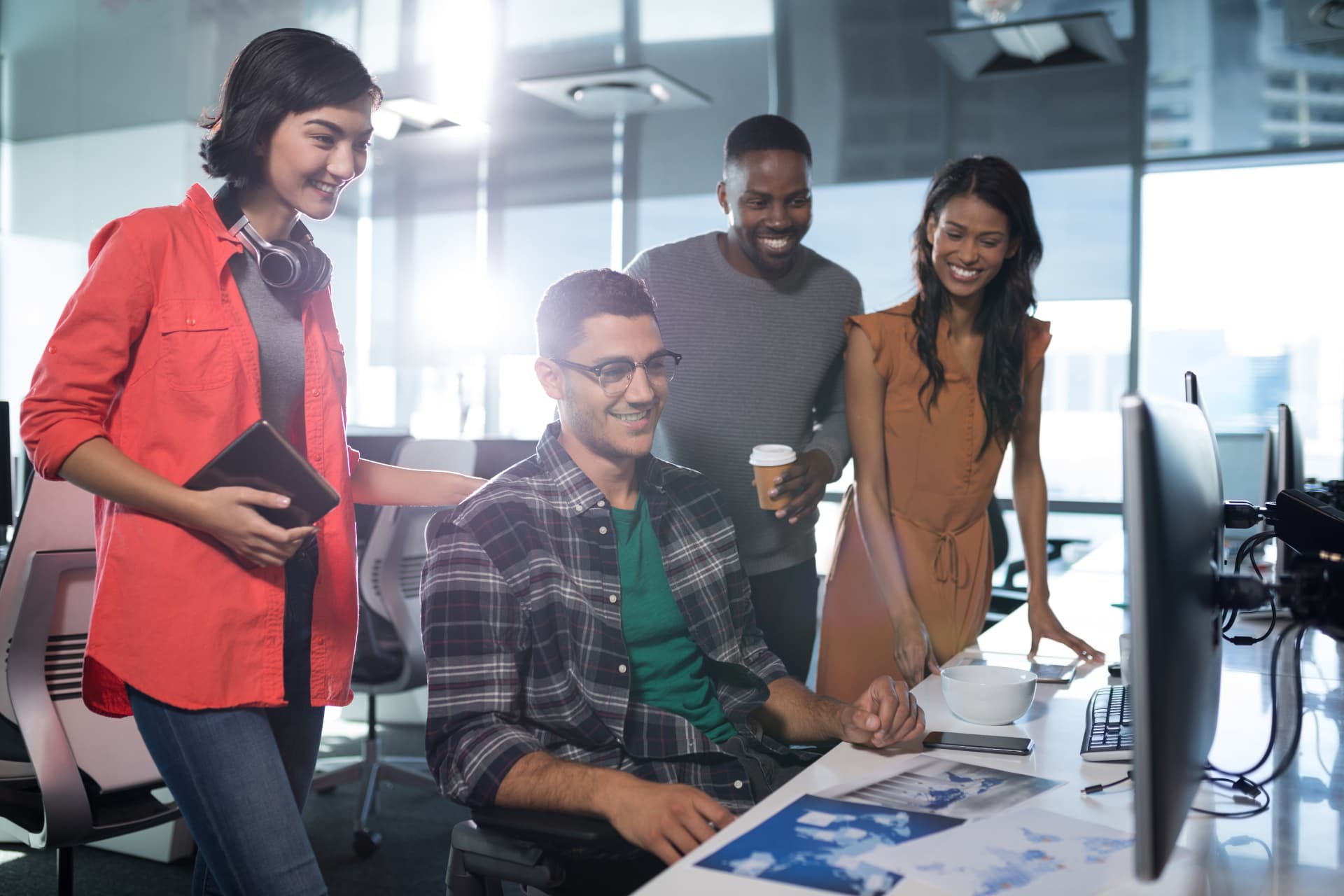 Four colleagues gathered around a desk reviewing work on a monitor in a bright studio.